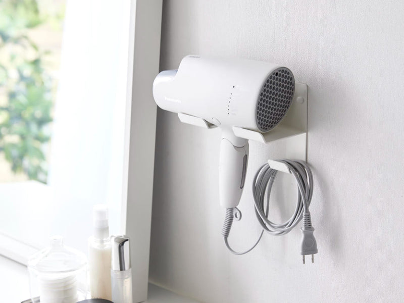 壁に取り付けられたスチール製のウォールドライヤーホルダーにヘアドライヤーが掛かっている様子