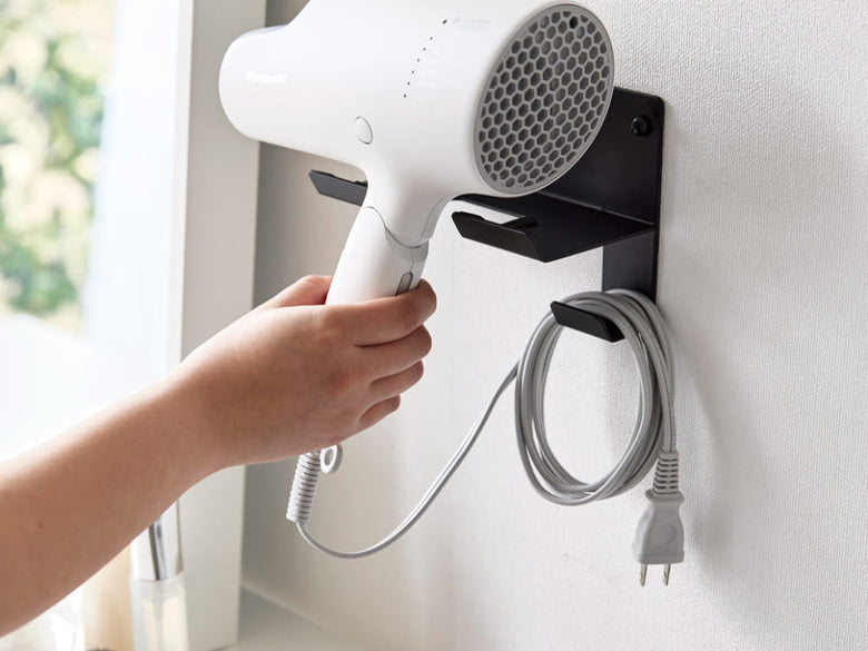 銀色のスチール製ウォールドライヤーホルダーが石こうボードの壁に取り付けられ、ヘアドライヤーを掛けている様子
