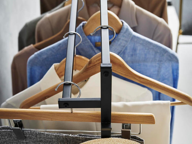 スチール製の「tower」収納力アップハンガーラックが木製の床に設置され、ハンガーや荷物が掛けられている様子