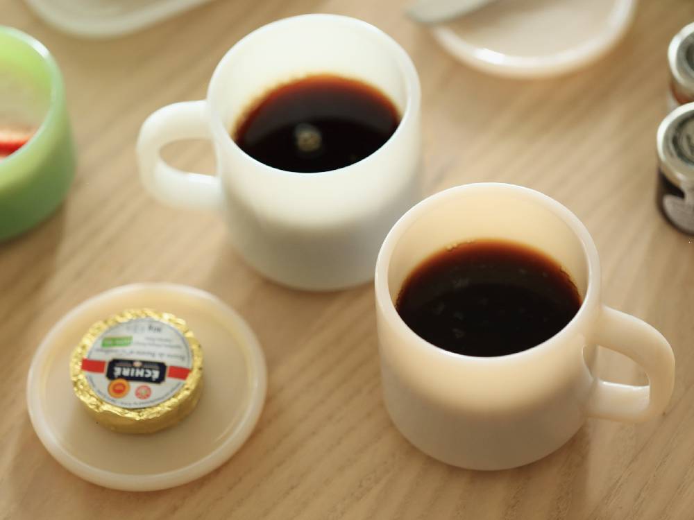 ミルクガラス製のマグカップ2個にコーヒーが注がれ、テーブルウェアとして並べられた様子