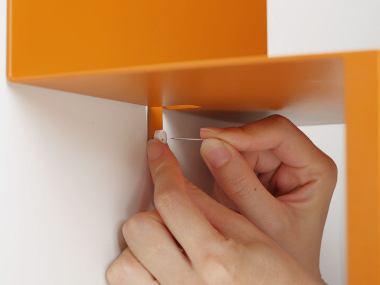 ideacoのスチール製ウォールテーブルB5が壁に取り付けられ、オレンジ色のプラスチック棚が配置されている様子