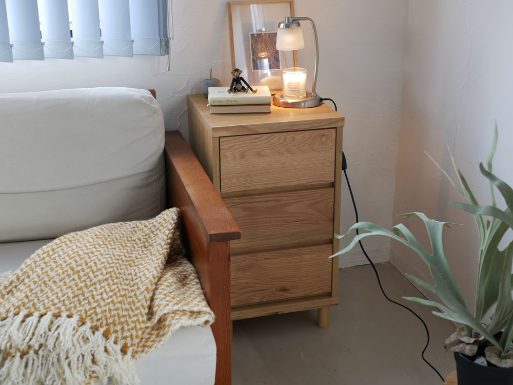 天然木製のチェストがベッドルームに置かれ、ホワイトオーク材の引き出しとラバーウッドの脚が特徴的な様子