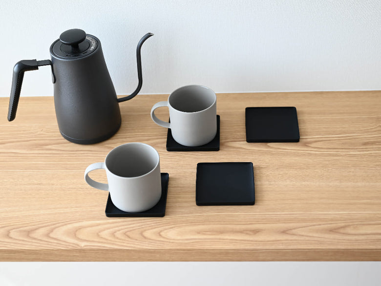 シリコーン製の【tower/タワー】立体コースターがカップやティーポット、電子機器と共にテーブル上に並べられています