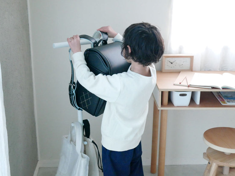 幼児がスマートランドセルスタンドを使い、バッグを掛けている清潔な部屋の様子