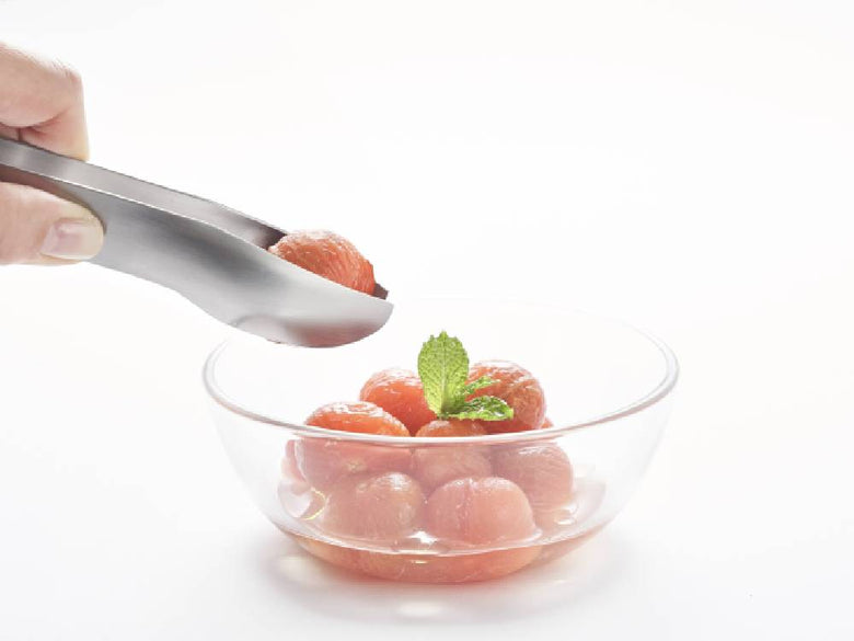 ステンレス製トングとスプーンが果物と一緒にボウルに置かれています